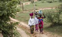 Women carry their belongings while walking towards their village. © FAO/Luis Tato